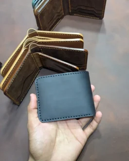 Hand holding a closed handcrafted full option black leather bifold wallet with hand-stitched border details.