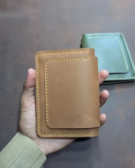A hand holding a closed tan handcrafted leather passport wallet and travel organizer featuring yellow perimeter stitching.